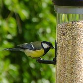 Koolmees met gele borst en zwarte kop eet zaden uit een gevulde doorzichtige vogelvoederbak.