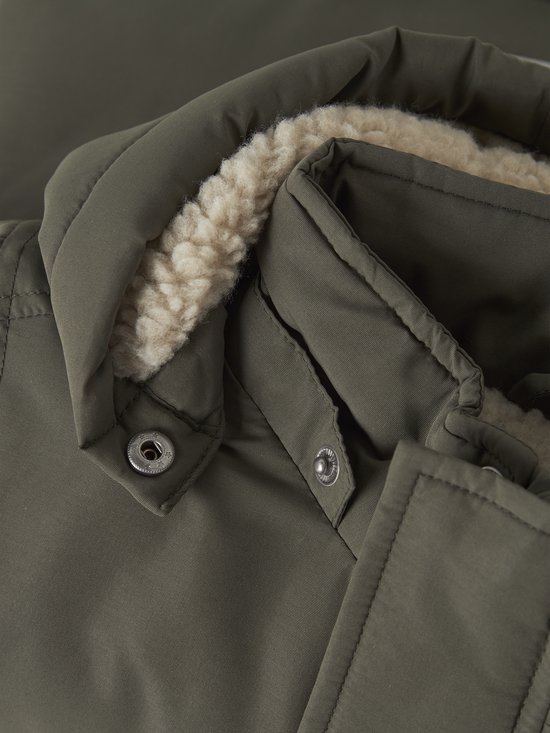 Close-up van de kraag van de olijfgroene parka met beige imitatiebont en metalen knoopsluitingen.