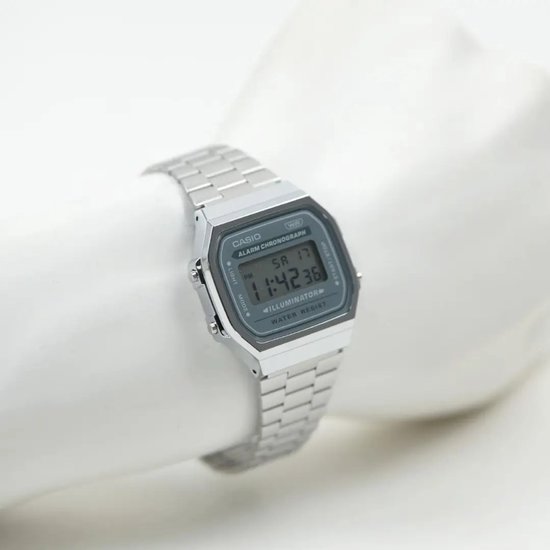 Zilverkleurig Casio digitaal horloge om een witte etalagepop, voorzien van een metalen band en vierkante kast.
