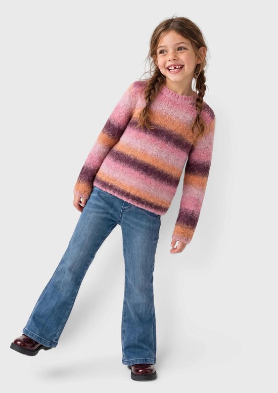 Meisje draagt een roze, oranje en paars gestreepte gebreide trui met blauwe jeans en donkerrode enkellaarzen.