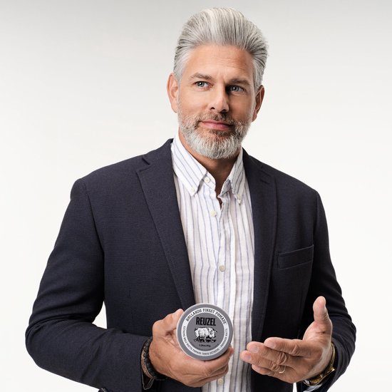 Man met grijs haar in een blauw colbert, houdt een blik Reuzel Extreme Hold Matte Pomade vast.
