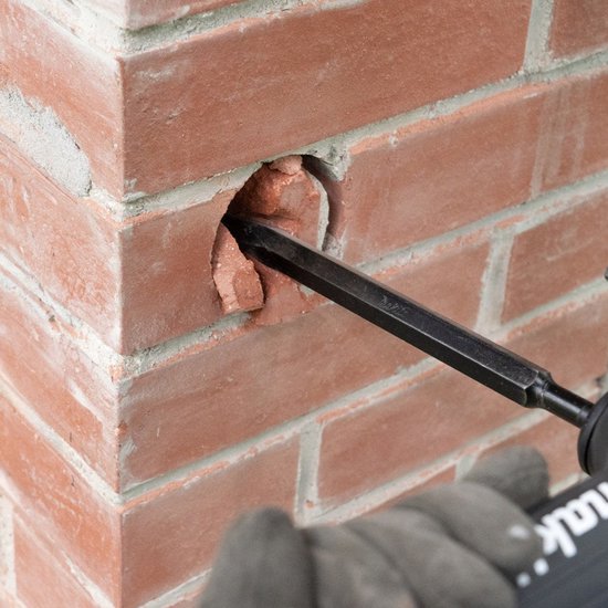 Een Makita-beitel verwijdert het binnenste van een gat in een bakstenen muur.