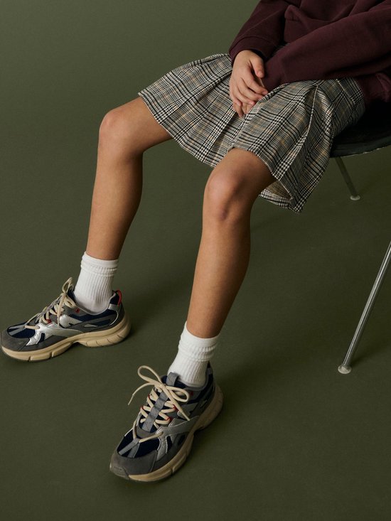 Detailopname van een geplooide rok met ruitpatroon en sneakers op een groene achtergrond.