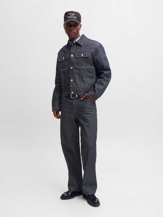 Model in een donkerblauw denim jack en straight fit jeans, aangevuld met een zwarte pet.