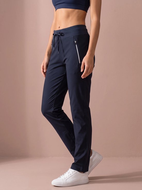 Model opzij gezien draagt donkerblauwe sportbroek met witte ritsen en koord in de taille.