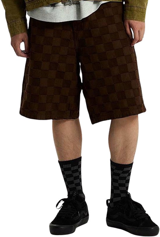 Model draagt zwarte Vans skate-sneakers met geblokte sokken en bruine short.