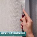 Hand met bordeauxrode nagellak snijdt lichtgrijze raamfolie met textielstructuur op maat.