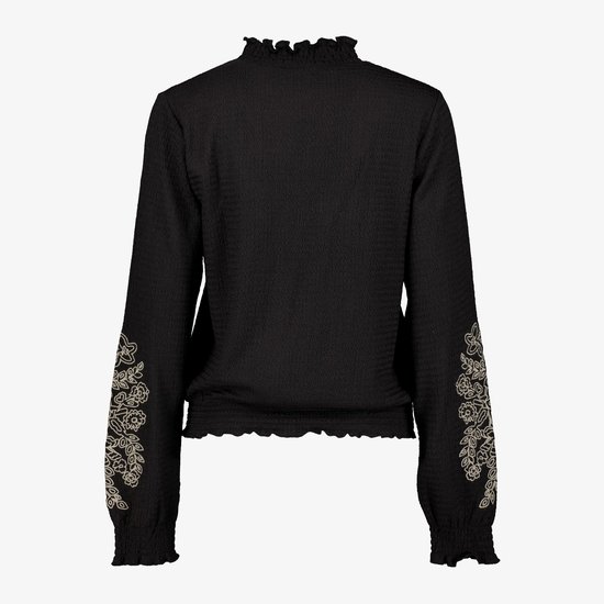 Zwarte blouse met lange mouwen, ruches bij de nek en mouwuiteinden, en geborduurde bloemen op de onderkant van de mouwen.