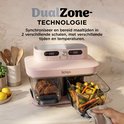 Roze Ninja DualZone airfryer op aanrecht, hand tilt glazen schaal met groenten en aardappelen uit de unit.