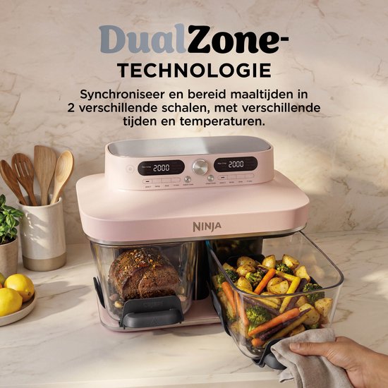 Roze Ninja DualZone airfryer op aanrecht, hand tilt glazen schaal met groenten en aardappelen uit de unit.