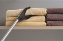 Grijper met gele grijppunten pakt een stapel beige handdoeken op een plank.