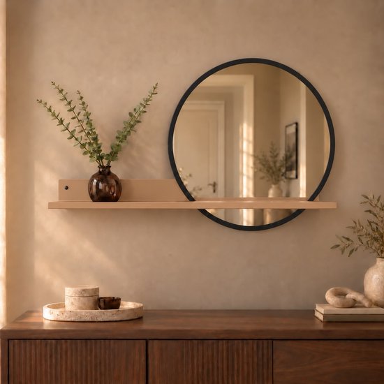 Ronde zwarte wandspiegel met beige wandplank en decoratie boven een houten dressoir.