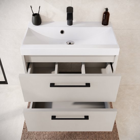 Bovenaanzicht van beige wastafelmeubel met twee geopende lades en een witte wastafel met zwarte kraan.