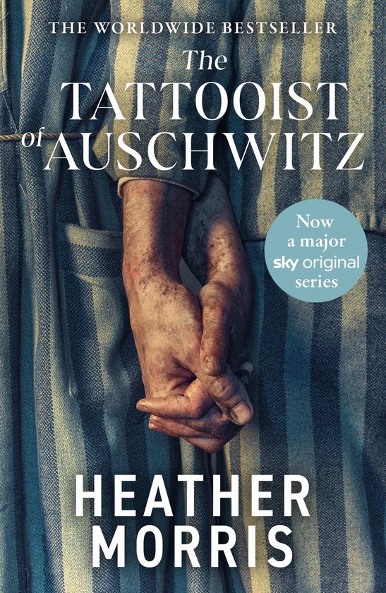 Boekcover: 'The Tattooist of Auschwitz' door Heather Morris, met twee handen die elkaar vasthouden voor een gestreepte stof. Nu een grote Sky Original serie.