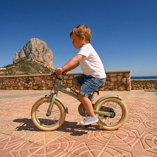Garçon sur un vélo d'enfant vert Deryan avec poignées et selle marron, t-shirt blanc et short en jean.