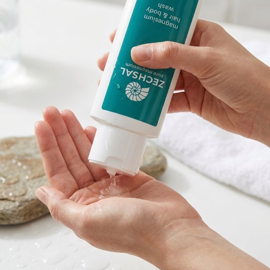 Hand die Zechsal magnesium hair & body wash in een hand schenkt, met water en stenen.
