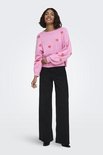 Model draagt roze trui met rode hartjesprint, lange mouwen en ronde hals, met zwarte broek.