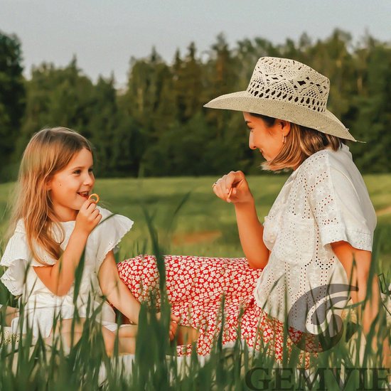 Een vrouw met een strooien hoed en een meisje met blond haar zitten in het gras.