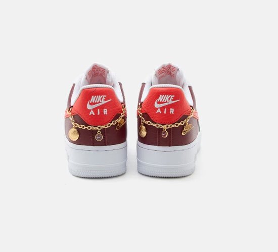Achterkant van witte Nike Air Force 1 sneakers met bordeauxrode en rode details, gouden ketting met bedeltjes en Nike Air logo's.