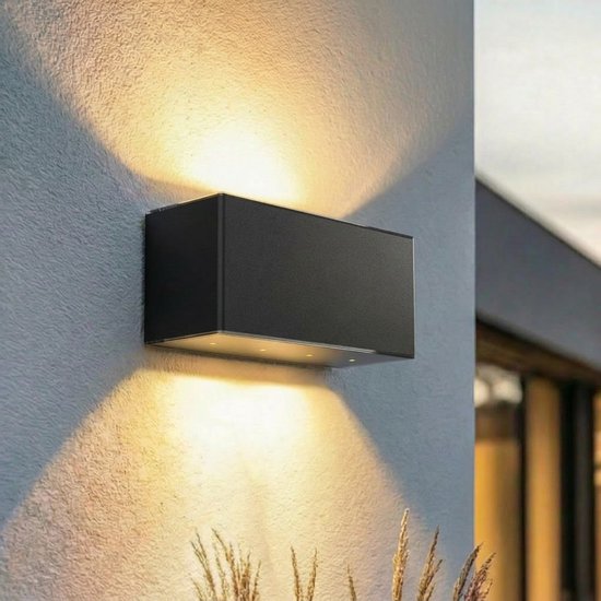 Zwarte rechthoekige buitenwandlamp monteert aan een muur en straalt warm licht naar boven en beneden.