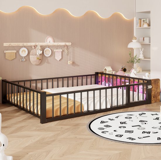Kinderbed met zwart metalen spijlenhek en houten hoofdeinde, opgemaakt met beddengoed in een kinderkamer met speelgoed.