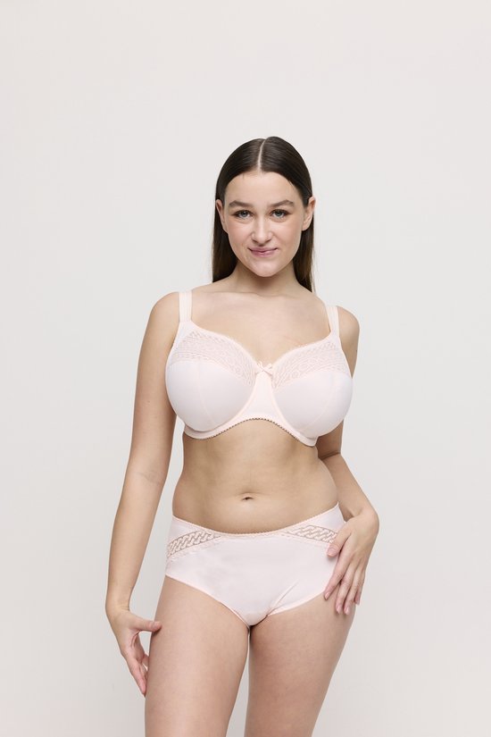 Model in een lichtroze beugelbh met kanten cups en een strikje, en een bijpassende broek met kanten details.