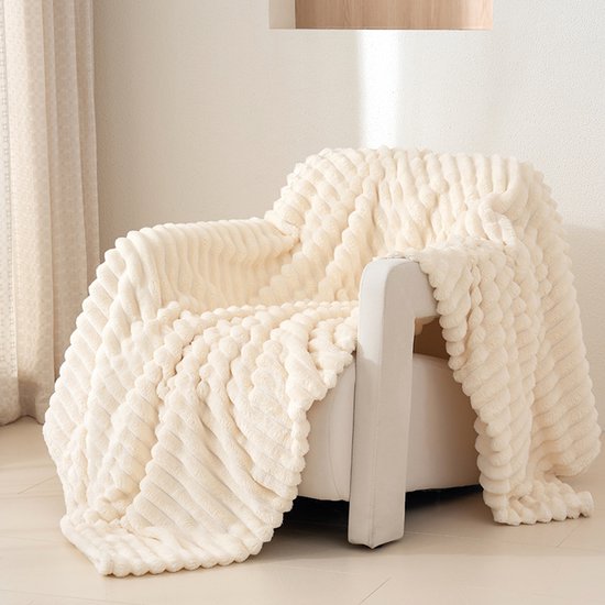 Couverture crème à motif côtelé, drapée sur un fauteuil blanc.