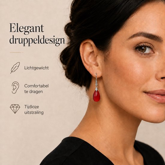 Close-up van een vrouw die zilverkleurige oorbellen met rode druppelvormige hangers draagt.
