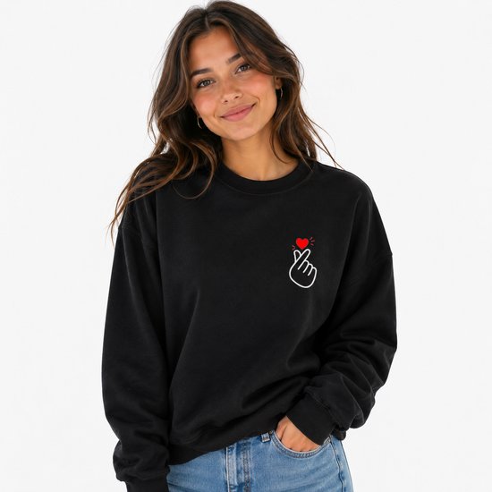 Sweatshirt noir avec une petite illustration brodée de cœur digital coréen sur le côté gauche, surmontée d'un cœur rouge.