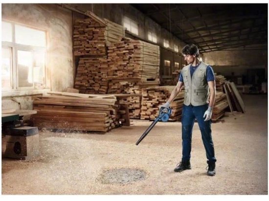 Man in beige vest blaast houtstof weg van de vloer met blauwe Bosch bladblazer in een werkplaats.