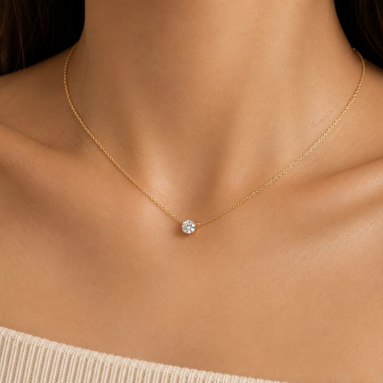 Gouden ketting met een enkele, schitterende zirkoon in het midden. Gedragen op de nek van een model.