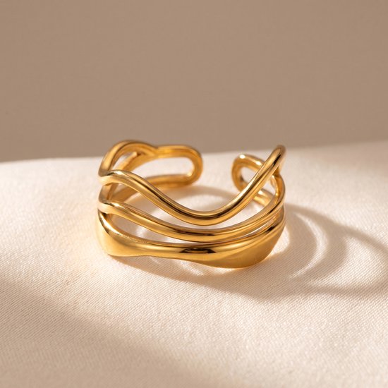 Gouden ring met meerdere golvende, overlappende lijnen, liggend op witte stof.