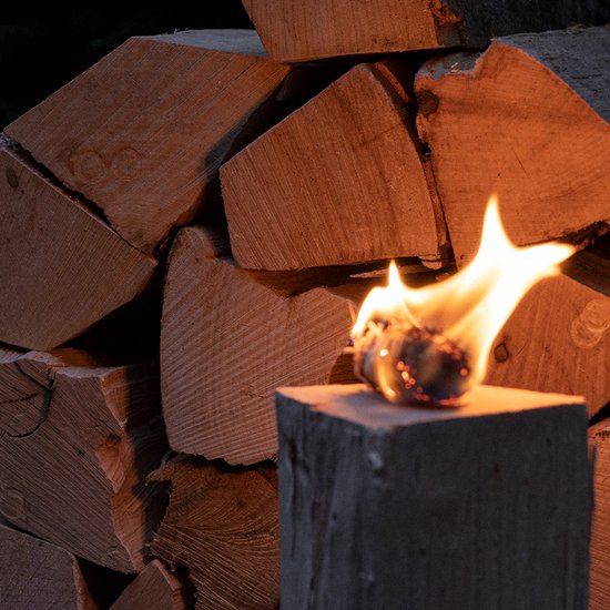 Een brandende fakkel voor een stapel bewerkt hout, met de gloed van het vuur op de houten stammen.