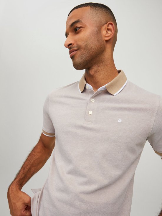 Man in een lichtgrijs polo shirt met beige kraag en witte en beige gestreepte mouwboorden. Geposeerd met handen in de zakken.