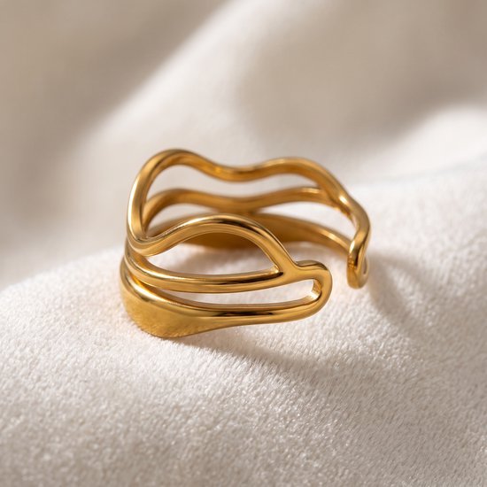Gouden ring met open uiteinden en golvende, overlappende lijnen, liggend op een witte stof.