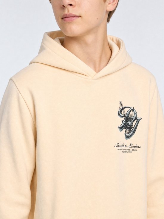 Close-up van een persoon in crèmekleurige hoodie met kraan-print op de borst en tekst 'Built to Endure'.