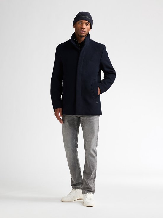 Model in een marineblauwe wollen mantel, grijze jeans en witte sneakers.