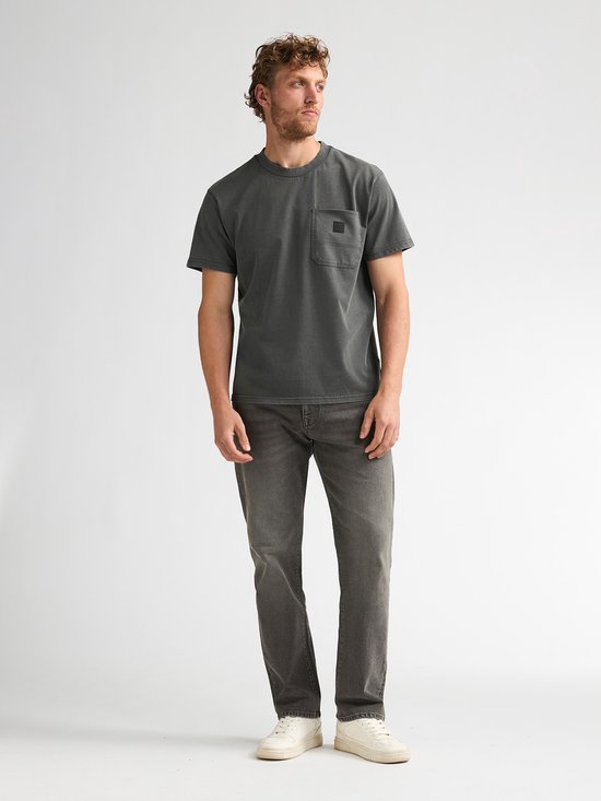 Man in donkergroen T-shirt met borstzakje en grijze jeans.