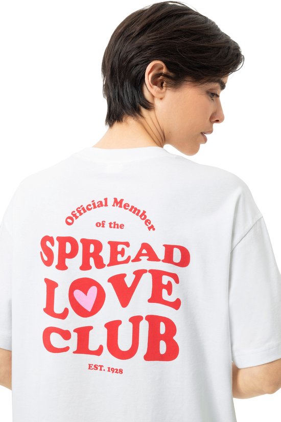 Close-up van de achterkant van een wit T-shirt met rode tekst 'Official Member of the SPREAD LOVE CLUB EST. 1928' en een hartje.