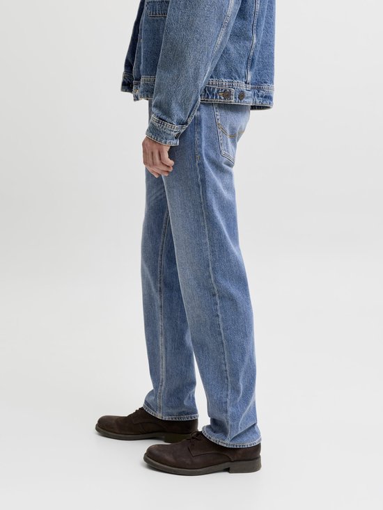 Zijaanzicht van een man die een spijkerbroek draagt in een medium wassing met een bruine leren riem en donkere schoenen.