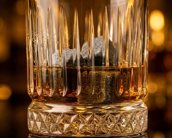 Whiskeystenen in een glas gevuld met amberkleurige whiskey, met bokeh achtergrond.