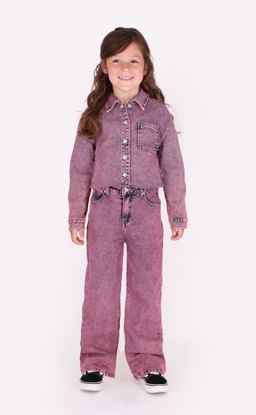Meisje met lang bruin haar draagt een roze spijkerblouse en bijpassende spijkerbroek. Ze draagt zwarte sneakers.