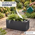 Een vrouw giet water in een donkergrijze plantenbak met een waterstop. Casaria logo.
