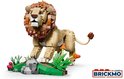 Gele lego leeuw met bruine manen, witte tanden, op een groene, stenen ondergrond met roze bloemen.