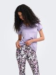 Model in paars sportshirt met V-hals en een veelkleurige legging met abstracte print. Ze trekt aan haar shirt.