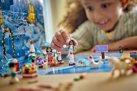 Meisje met krullend haar speelt met LEGO Friends kerstkalender. Op de tafel: sneeuwpoppen, pinguïns, een kerstboom en skifiguurtjes.