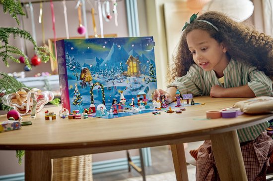 Meisje met krullend haar speelt met een LEGO Friends kerstkalender met winterse taferelen, huisjes en figuurtjes.