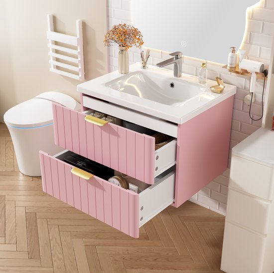 Meuble de salle de bain rose avec deux portes côtelées ouvertes, lavabo blanc et poignées dorées.
