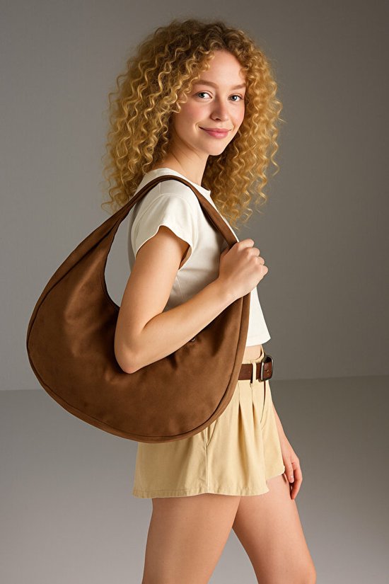 Model met lichtbruine suède schoudertas, beige top en beige short.