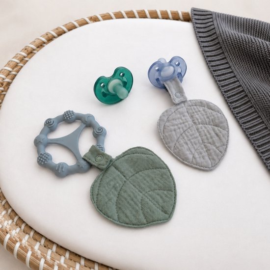 Twee blad-vormige bonding leafs (groen en grijs), een groene en een blauwe fopspeen en een grijze bijtring in een mandje.